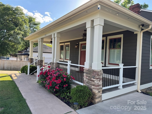 view of exterior entry featuring covered porch, ceiling fan, a chimney, and fence