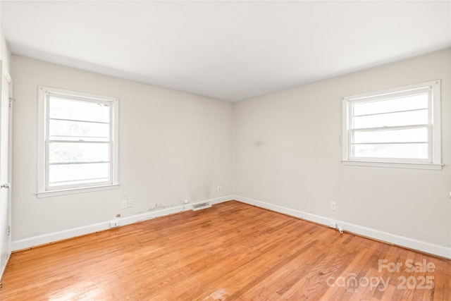 empty room featuring visible vents, a healthy amount of sunlight, light wood finished floors, and baseboards