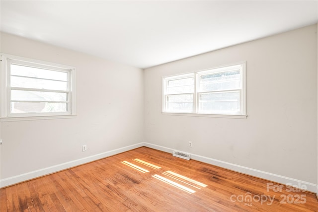 empty room featuring visible vents, wood finished floors, a healthy amount of sunlight, and baseboards