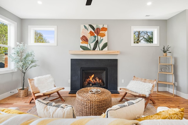 living area with wood finished floors, recessed lighting, a warm lit fireplace, and baseboards
