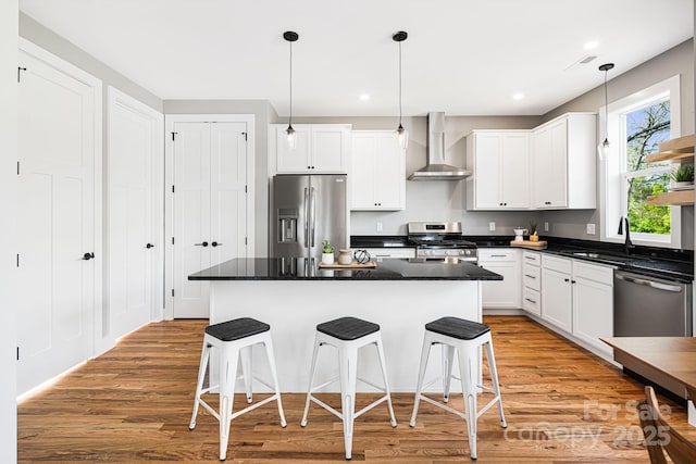 kitchen featuring light wood finished floors, a sink, stainless steel appliances, wall chimney exhaust hood, and a breakfast bar area