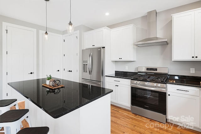 kitchen with a breakfast bar, stainless steel appliances, white cabinets, and wall chimney exhaust hood