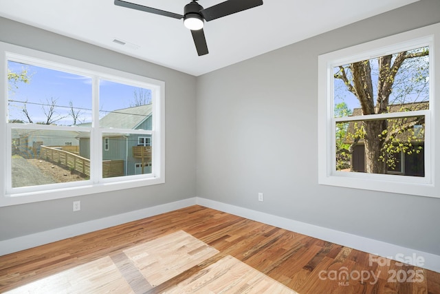 unfurnished room featuring baseboards, visible vents, wood finished floors, and a wealth of natural light