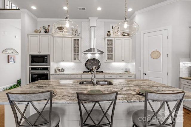 kitchen with stainless steel appliances, a breakfast bar, a sink, visible vents, and wall chimney range hood