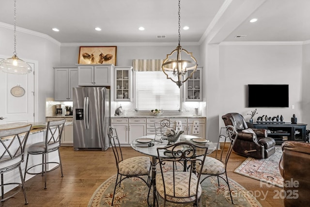 dining space with crown molding, wood finished floors, visible vents, recessed lighting, and an inviting chandelier