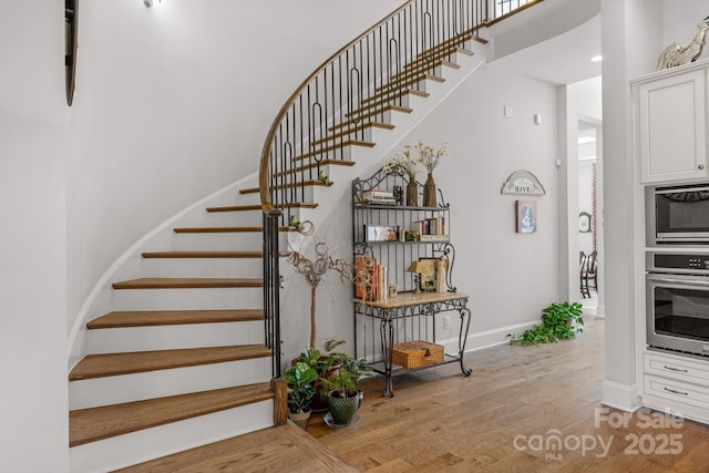 stairway with a high ceiling, baseboards, and wood finished floors