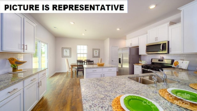 kitchen with tasteful backsplash, a sink, white cabinetry, wood finished floors, and stainless steel appliances