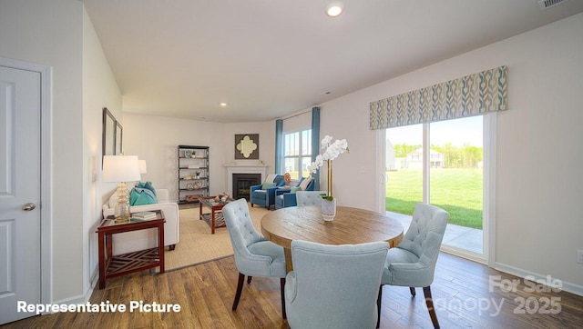 dining room with visible vents, a glass covered fireplace, wood finished floors, baseboards, and recessed lighting