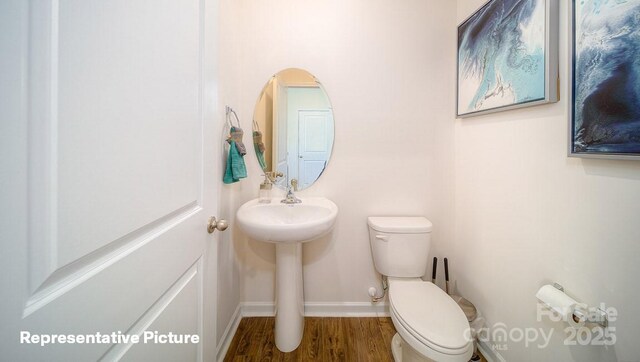 half bath with toilet, baseboards, and wood finished floors