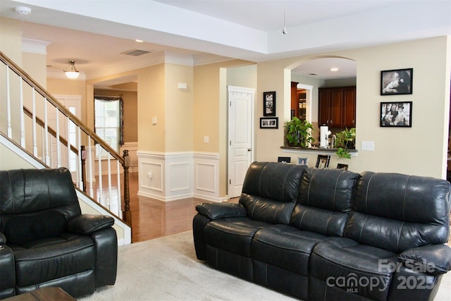 carpeted living area with visible vents, wainscoting, arched walkways, ornamental molding, and stairs