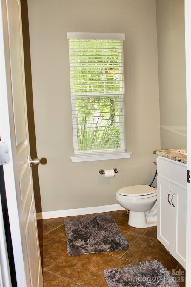 half bathroom with tile patterned flooring, toilet, a wealth of natural light, and vanity