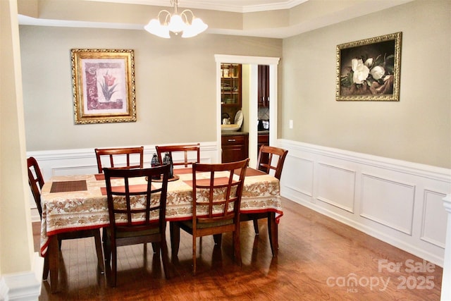 dining room with a notable chandelier, ornamental molding, wainscoting, a decorative wall, and wood finished floors