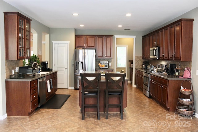 kitchen featuring glass insert cabinets, decorative backsplash, appliances with stainless steel finishes, a kitchen island, and recessed lighting