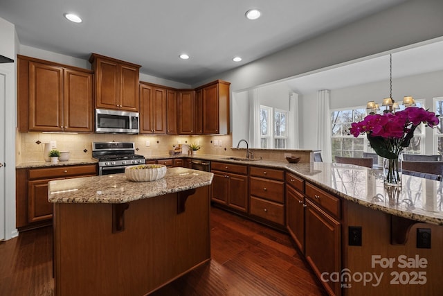 kitchen featuring light stone countertops, stainless steel appliances, a kitchen bar, a sink, and a center island