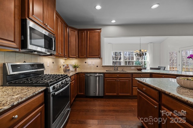 kitchen featuring light stone countertops, an inviting chandelier, stainless steel appliances, a sink, and dark wood-style floors