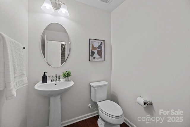 half bathroom featuring wood finished floors, toilet, a sink, baseboards, and visible vents