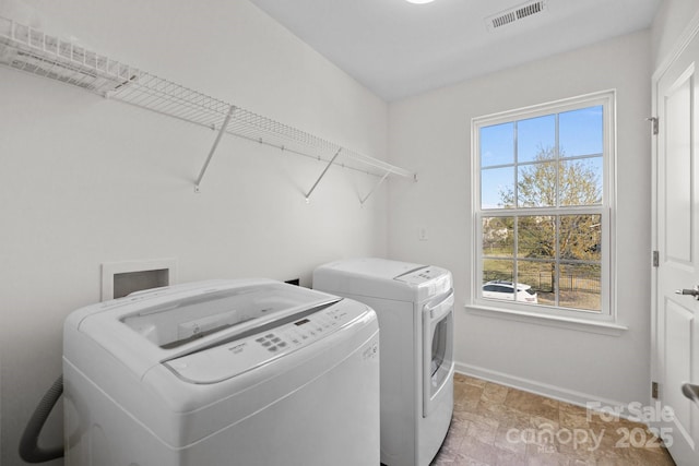 washroom featuring washing machine and clothes dryer, laundry area, visible vents, stone finish floor, and baseboards
