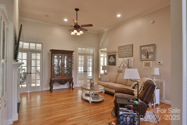living area featuring crown molding, light wood-type flooring, french doors, a ceiling fan, and a high ceiling