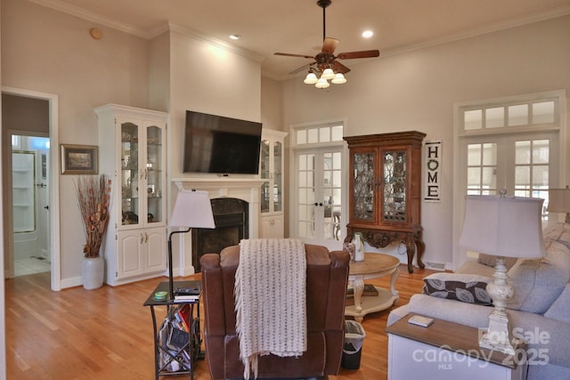living area with light wood-style flooring, a ceiling fan, french doors, and crown molding