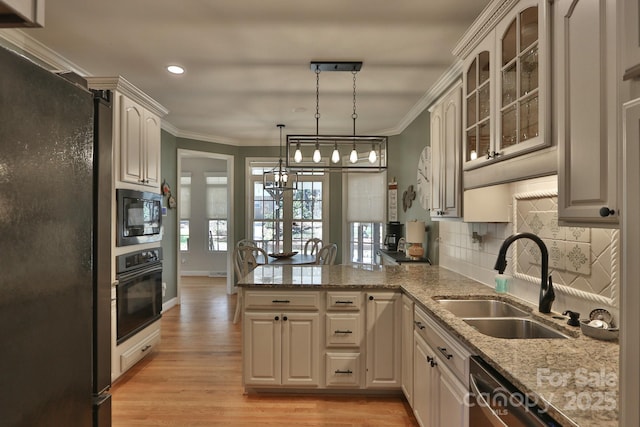 kitchen featuring a sink, black appliances, light wood-style flooring, backsplash, and a peninsula