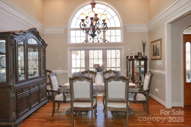 dining area featuring a high ceiling, a notable chandelier, baseboards, arched walkways, and wood finished floors