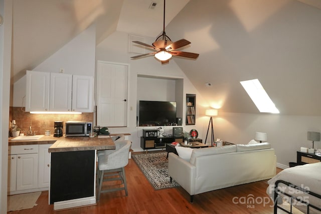 living room with high vaulted ceiling, ceiling fan, visible vents, a skylight, and wood finished floors