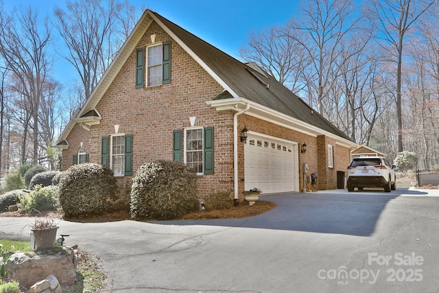 view of side of home with roof with shingles, aphalt driveway, brick siding, and a garage
