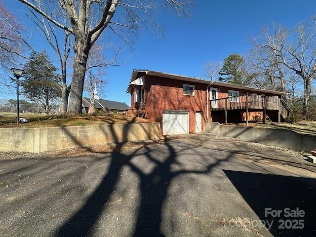 exterior space with a garage, brick siding, aphalt driveway, and a deck