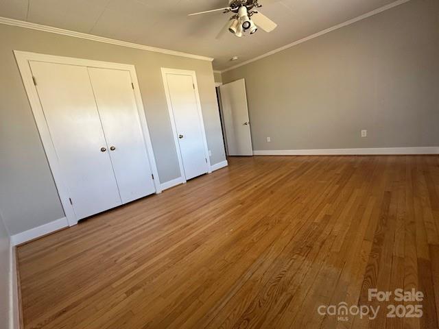 unfurnished bedroom featuring ornamental molding, baseboards, multiple closets, and wood finished floors