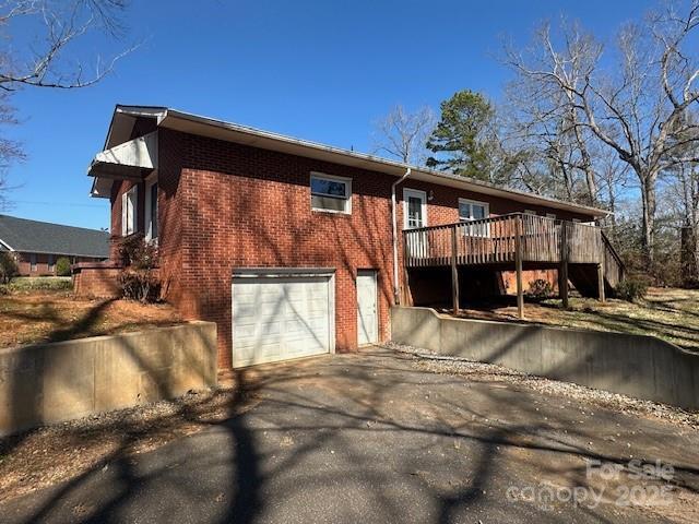 view of side of property featuring driveway, brick siding, a garage, and a deck