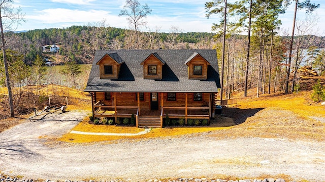 log-style house with covered porch, a wooded view, and roof with shingles
