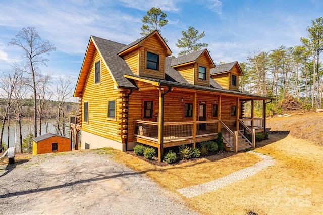 view of front of home with an outdoor structure, a shingled roof, covered porch, and log siding