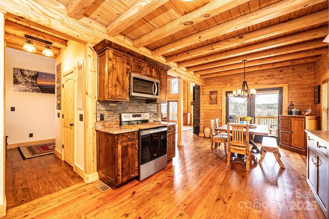 kitchen with brown cabinetry, appliances with stainless steel finishes, light wood-type flooring, wooden ceiling, and an inviting chandelier