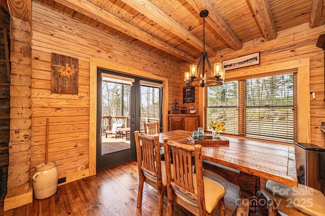 dining area with wood walls, beam ceiling, a chandelier, hardwood / wood-style flooring, and french doors
