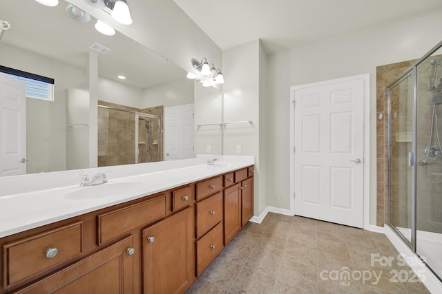 full bath with visible vents, a shower stall, baseboards, double vanity, and a sink
