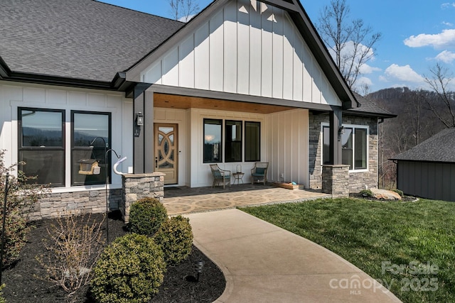 exterior space with board and batten siding, a front yard, a shingled roof, and stone siding