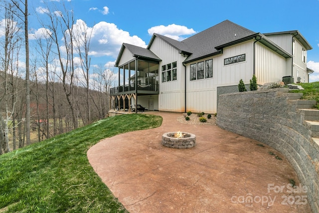 rear view of property featuring a shingled roof, a fire pit, a sunroom, a yard, and a patio