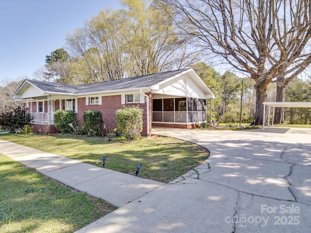 single story home featuring a sunroom, concrete driveway, a front lawn, brick siding, and an attached carport
