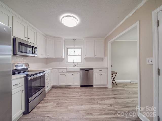 kitchen featuring white cabinetry, ornamental molding, a sink, light wood-style floors, and appliances with stainless steel finishes