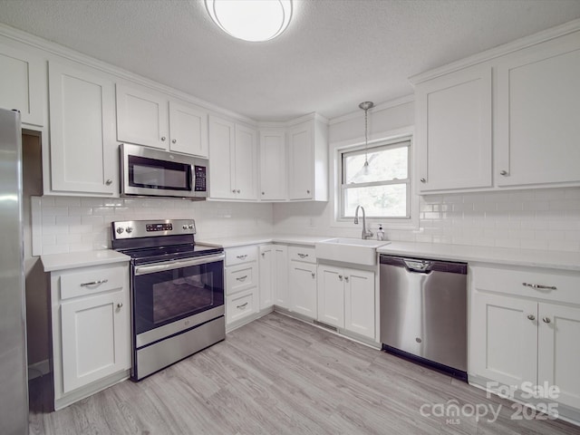 kitchen with light countertops, a sink, stainless steel appliances, and light wood finished floors