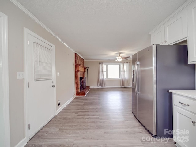 kitchen featuring stainless steel fridge, a fireplace, ceiling fan, ornamental molding, and white cabinetry