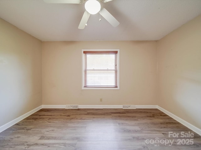 unfurnished room featuring baseboards, visible vents, ceiling fan, and wood finished floors