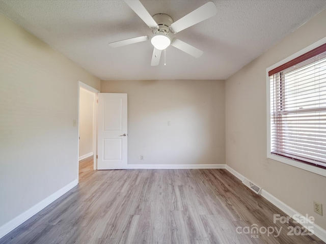 empty room with light wood finished floors, a textured ceiling, baseboards, visible vents, and ceiling fan