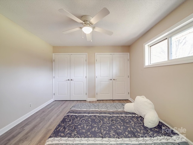 bedroom featuring wood finished floors, a textured ceiling, multiple closets, baseboards, and ceiling fan