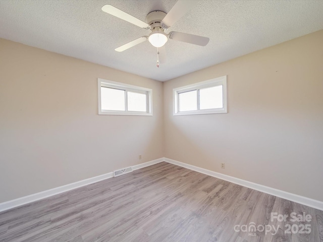spare room with baseboards, light wood-style floors, a textured ceiling, and visible vents