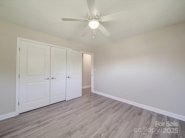 unfurnished bedroom with light wood-style flooring, baseboards, a closet, and a textured ceiling