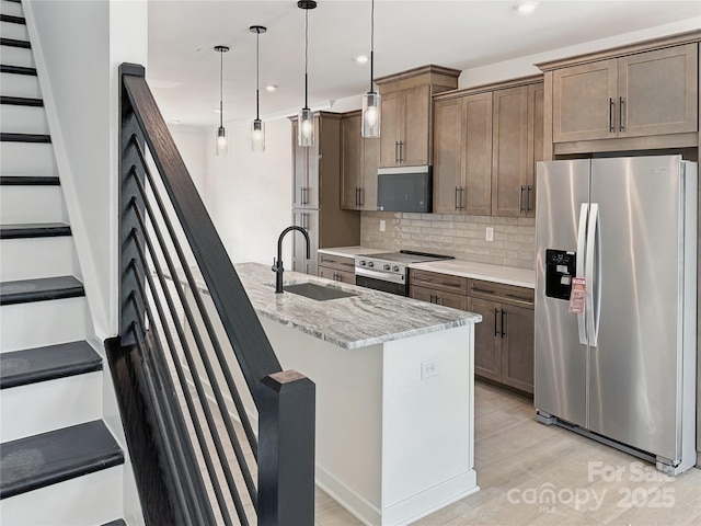 kitchen with light stone counters, decorative backsplash, a sink, appliances with stainless steel finishes, and light wood-style floors