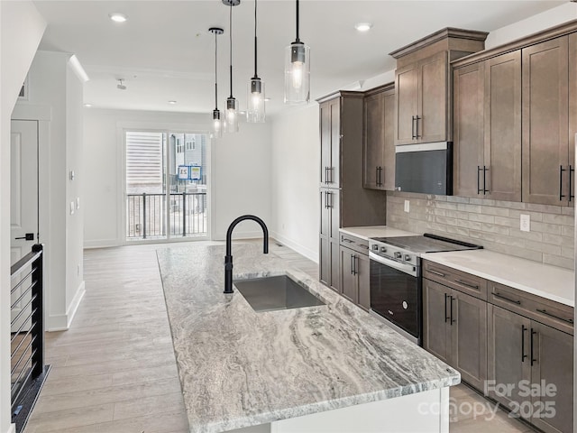 kitchen featuring a sink, tasteful backsplash, electric range, baseboards, and an island with sink