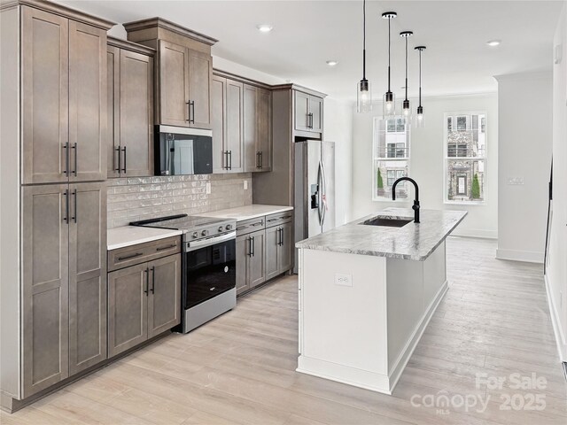 kitchen with a kitchen island with sink, a sink, stainless steel appliances, decorative backsplash, and ornamental molding