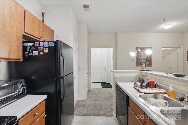 kitchen with light countertops, a sink, visible vents, black appliances, and brown cabinetry